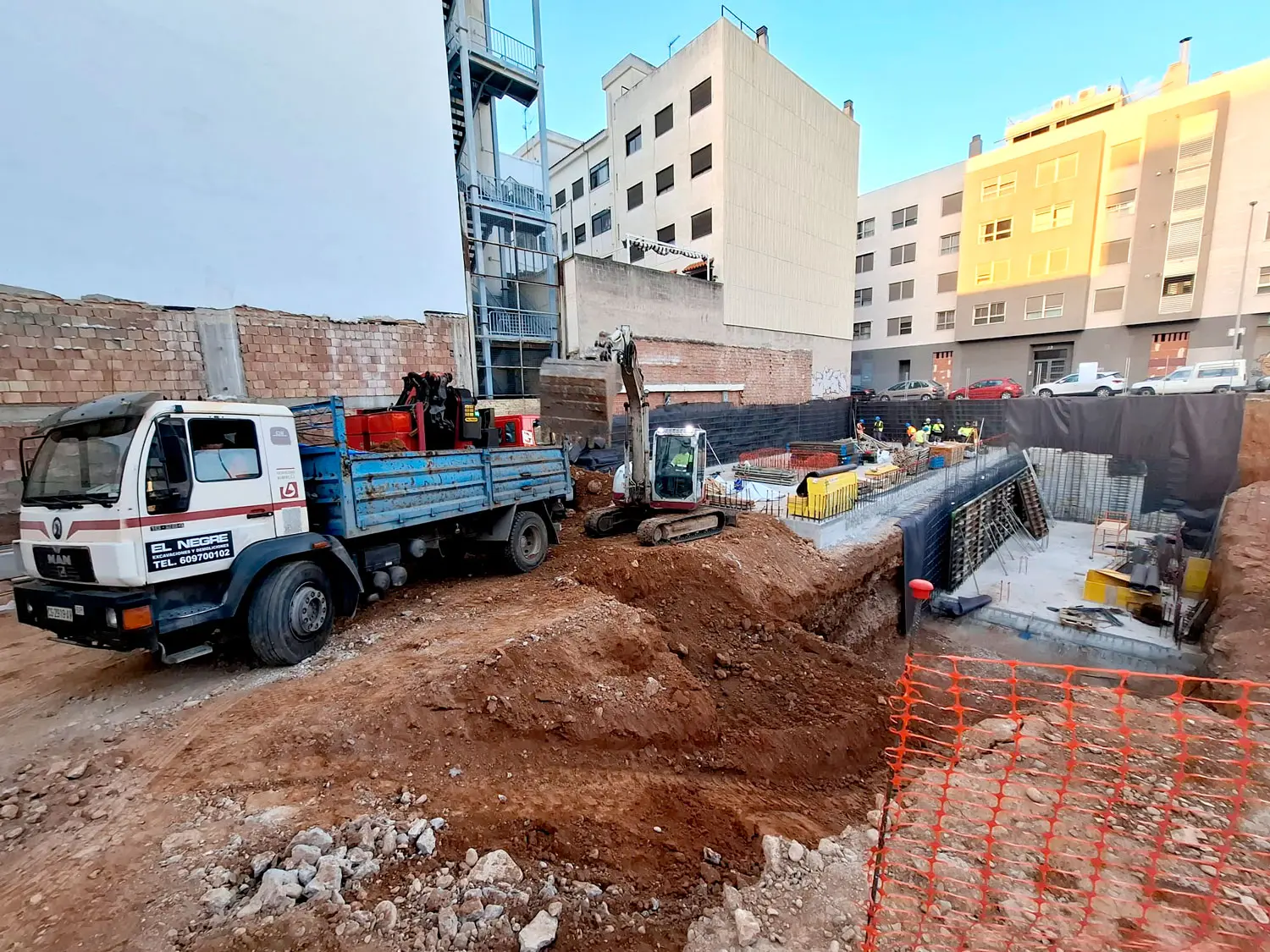 Trwająca budowa budynku Luz – etap wykonywania fundamentów Koparka i ciężarówka na placu budowy budynku Luz, gdzie pracownicy zajmują się wykonywaniem fundamentów.