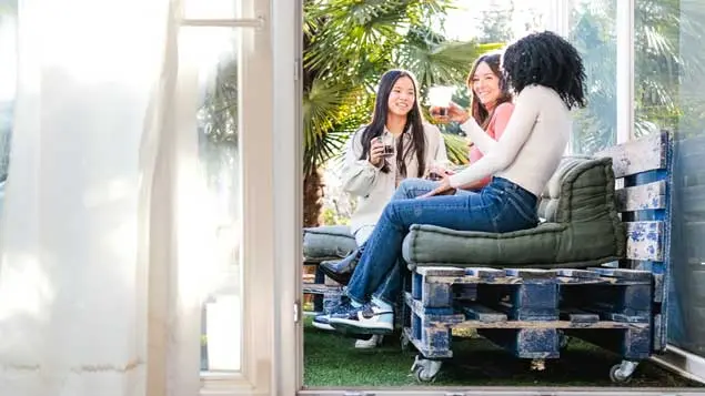 Low-cost terrace with recycled pallets and a youthful atmosphere Three girls chatting on a low-cost terrace with sofas made from pallets and cushions.