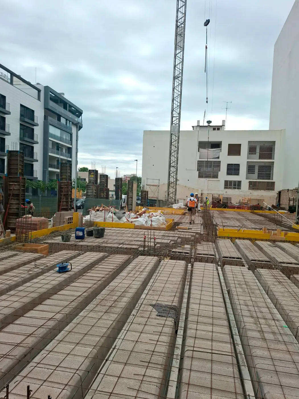 Postęp prac budowlanych przy budynku Luz – robotnicy przy stropie Robotnicy pracujący przy budowie budynku Luz na stropie z wykorzystaniem dźwigu i konstrukcji betonowych