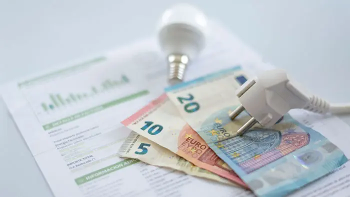 Banknoty euro na rachunku za prąd obok wtyczki i żarówki, symbolizujące oszczędność energii dzięki systemom aerotermicznym